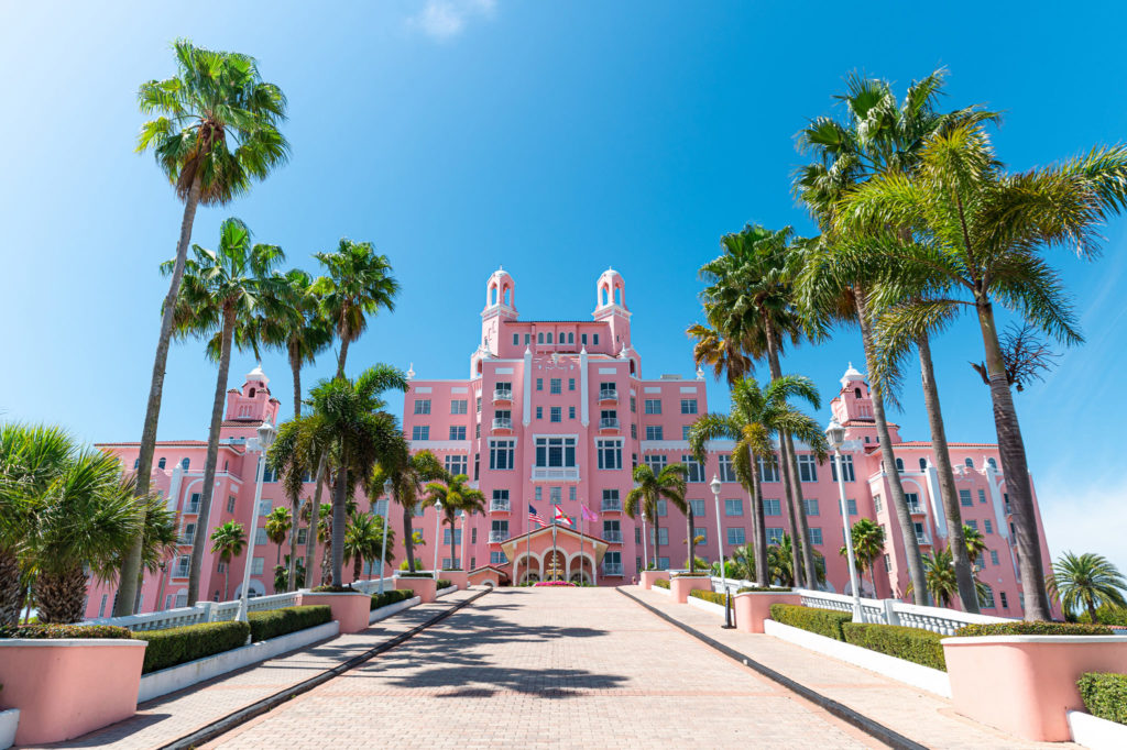 Exterior of The Don CeSar hotel in St. Pete Beach, Florida, known as the “Pink Palace,” surrounded by palm trees under a clear blue sky.