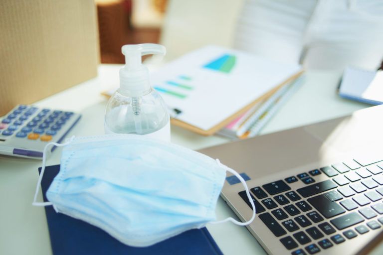 medical mask and hand disinfectant on table in home office