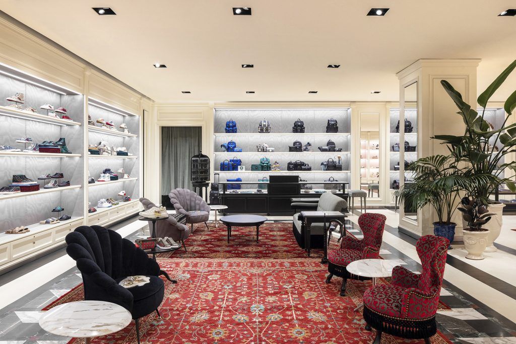 Gucci boutique interior with handbags on illuminated shelves, red patterned carpet and seating areas with velvet chairs.