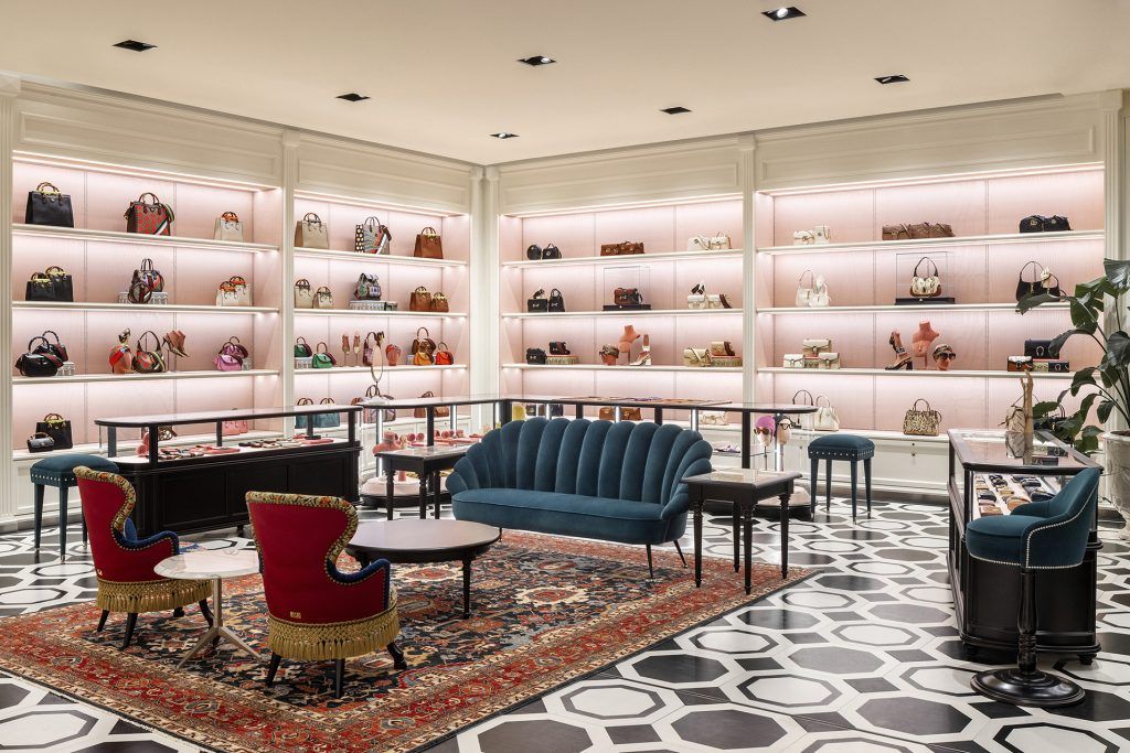 Interior view of a Gucci boutique with handbags displayed on backlit shelves and a seating area with patterned flooring.