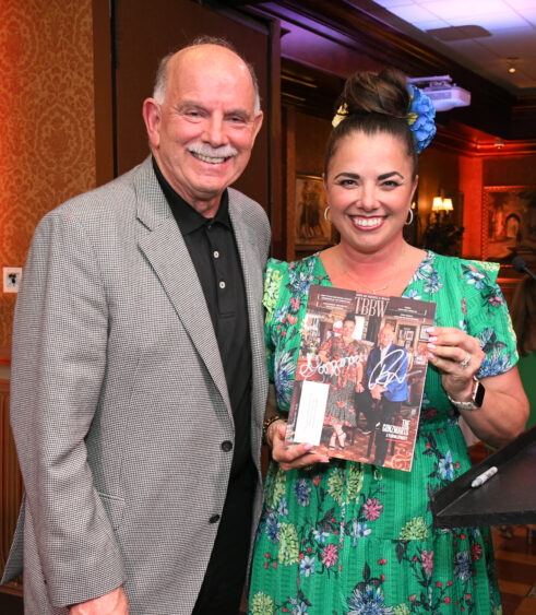 Andrea Gonzmart Williams holds a signed copy of Tampa Bay Business & Wealth magazine while standing next to a man in a gray blazer at an event.