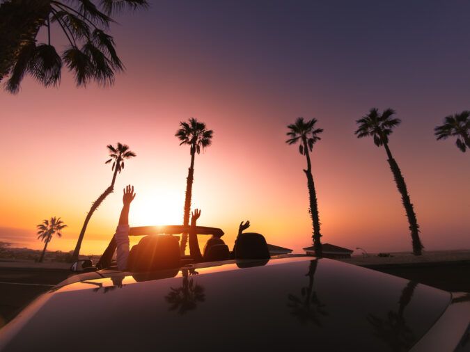 Happy young couple doing road trip in tropical city - Travel people having fun driving in trendy convertible car discovering new places - Relationship and youth vacation lifestyle concept