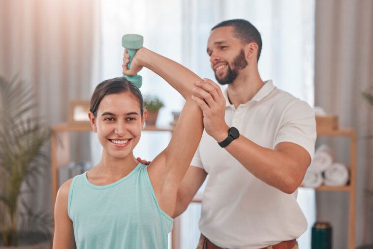 Physical therapy, smile and exercise for shoulder pain of a happy woman with a chiropractor employee. Arm workout weight lifting of a patient feeling relax after a chiropractic and dumbbell lifting