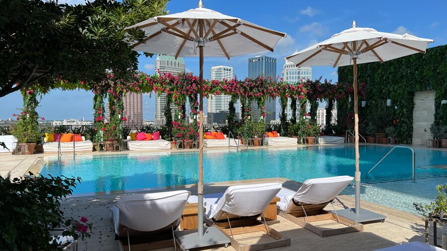 Pool deck at The Tampa Edition overlooking Water Street, featuring white loungers and lush greenery