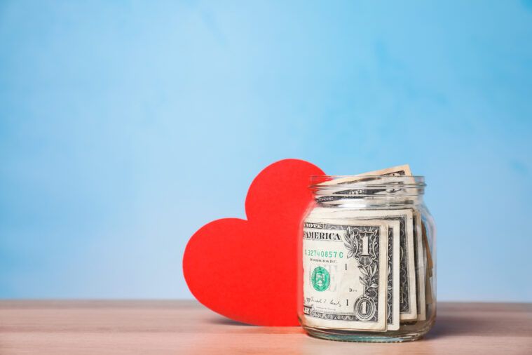Red heart and donation jar with money on table against color background. Space for text