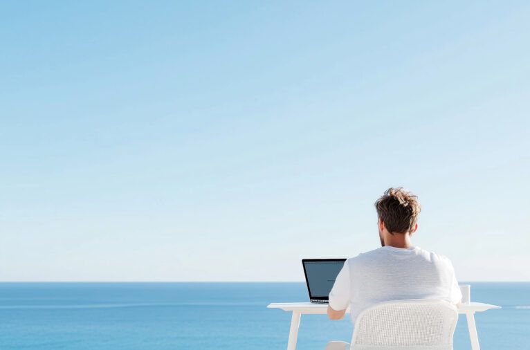 Man working remotely with laptop by the ocean under clear blue sky