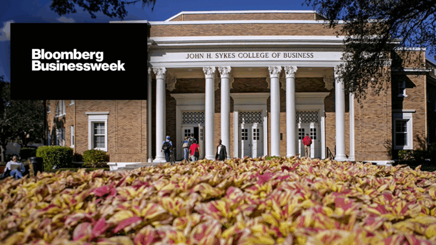 Front entrance of the University of Tampa’s John H. Sykes College of Business with students walking across campus, overlaid with the Bloomberg Businessweek logo.