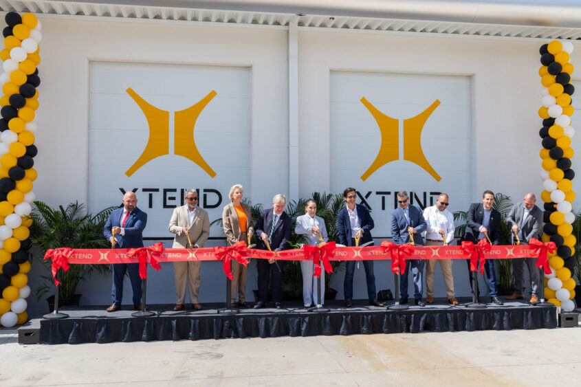 Group of leaders, including Tampa Mayor Jane Castor, cutting a red ribbon during the grand opening ceremony at XTEND’s U.S. headquarters, with the XTEND logo and balloon columns in the background.