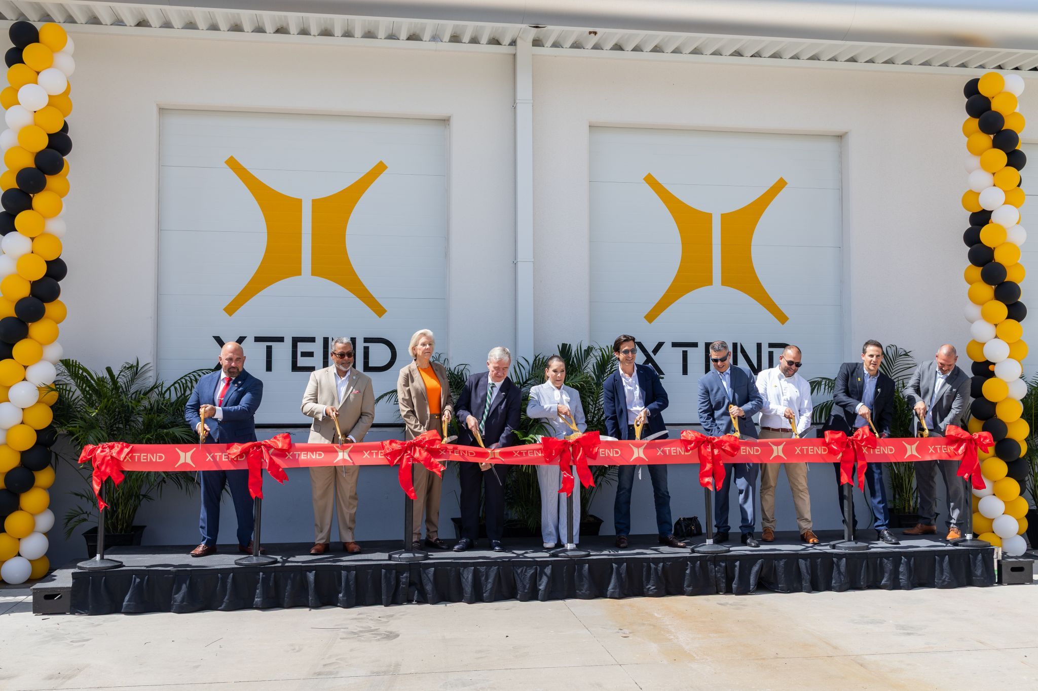 Group of leaders, including Tampa Mayor Jane Castor, cutting a red ribbon during the grand opening ceremony at XTEND’s U.S. headquarters, with the XTEND logo and balloon columns in the background.
