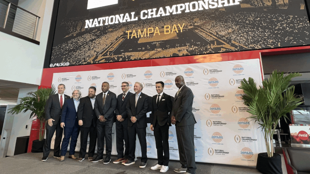 Local and sports leaders stand on stage in front of a “National Championship Tampa Bay” backdrop during the announcement that Raymond James Stadium will host the 2029 College Football Playoff National Championship.