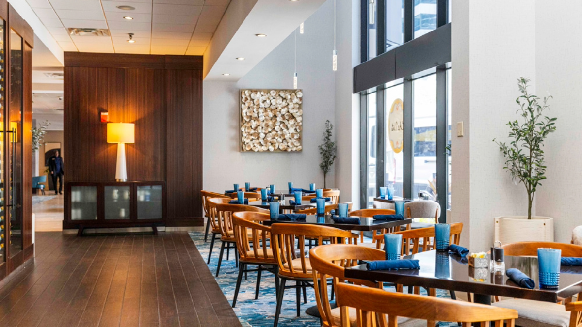 Interior of Che Vita restaurant at Hilton Tampa Downtown featuring wood tables, blue glassware and natural light from floor-to-ceiling windows