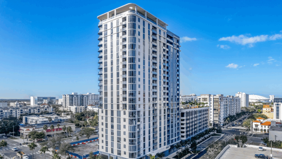 A 23-story mixed-use tower named EVO rises above downtown St. Petersburg, featuring modern architecture, glass balconies, and surrounding midrise developments under clear blue skies.