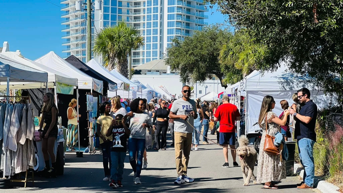 Crowds walk between rows of white vendor tents at a Tampa Bay Markets event in downtown Tampa, with local businesses selling food, crafts and clothing under clear blue skies.