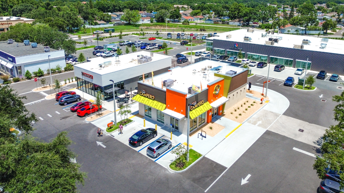 Aerial view of a newly built Pollo Campero restaurant in West Tampa, located next to a Chipotle and across from a Target and Lowe’s shopping center on West Waters Avenue. Several cars are parked in the lot under a bright, sunny sky.