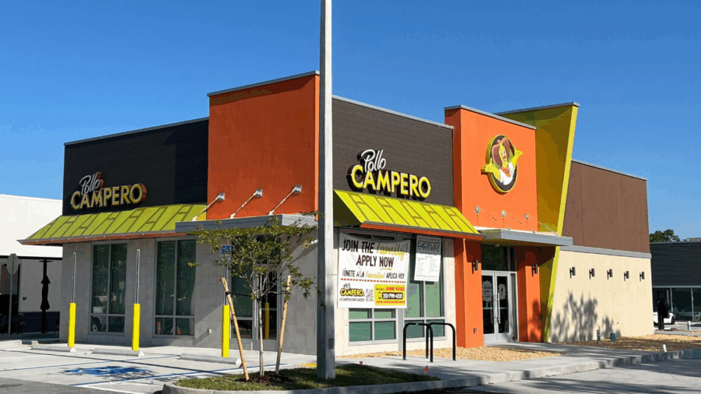 Front view of the newly built Pollo Campero restaurant on West Waters Avenue in West Tampa, featuring bright orange and yellow exterior accents under a clear blue sky.