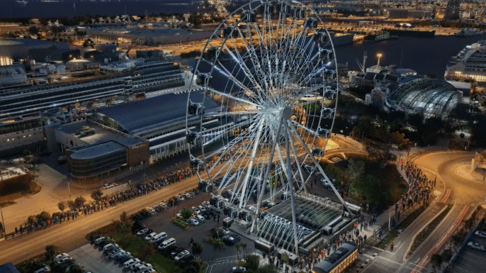 Nighttime rendering of the Tampa WOW! observation wheel in the Channel District, surrounded by pedestrians, parked cars, and illuminated waterfront attractions including The Florida Aquarium.