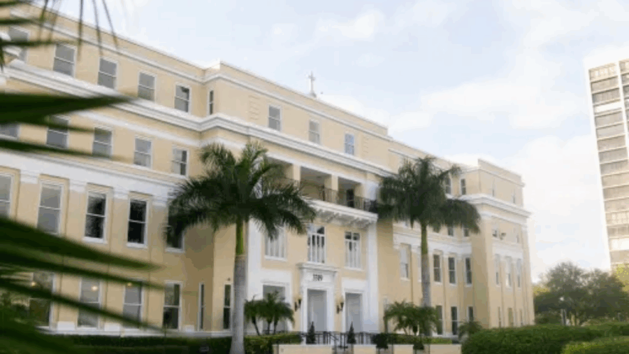 The front entrance of the Academy of the Holy Names on Bayshore Boulevard in South Tampa, framed by palm trees and early morning light.
