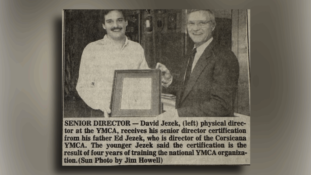 Newspaper clipping showing David Jezek receiving his senior director certification from his father, symbolizing a lifetime of service to the YMCA.