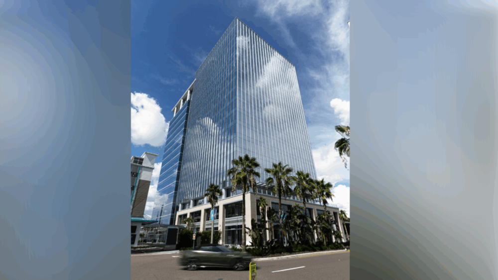 Exterior of the glass Midtown East office tower in Tampa, with palm trees and blue sky.