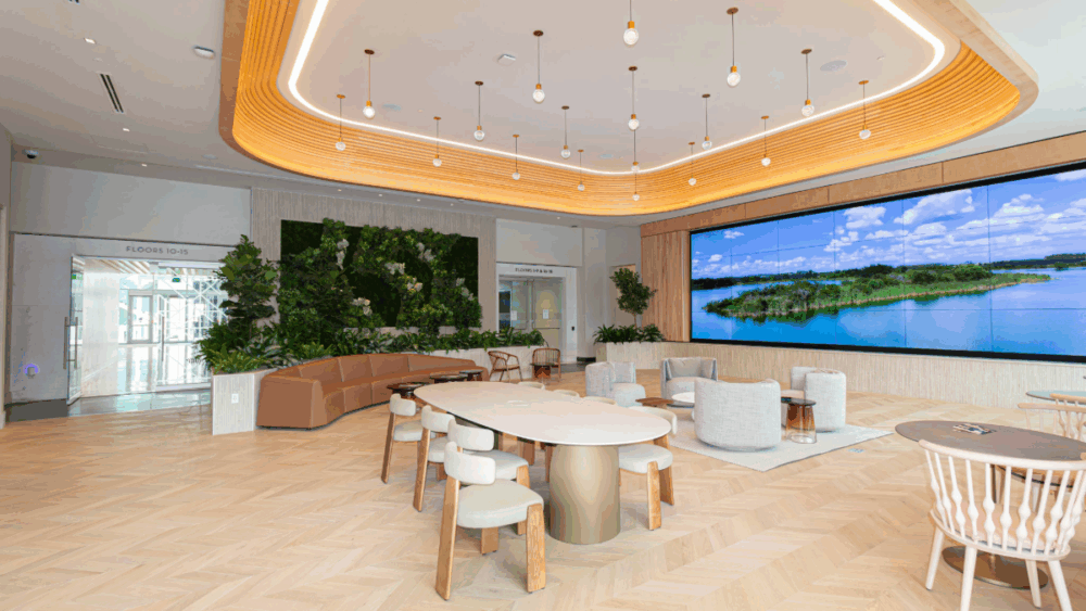 Interior view of Midtown East’s lobby with natural wood tones, plant wall, modern furniture and large video wall.