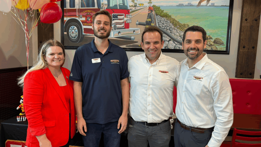Four people stand together inside the new Firehouse Subs restaurant in Clearwater, smiling for a photo in front of a mural featuring a Clearwater Fire & Rescue truck.
