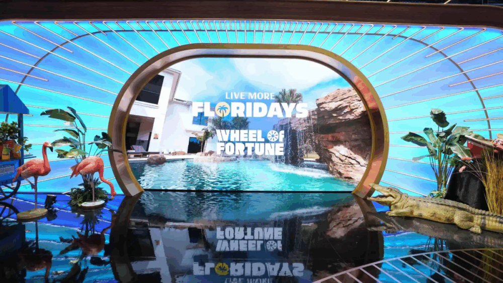 Wheel of Fortune set decorated for “Live More Floridays” week, featuring tropical props and a Florida pool backdrop.