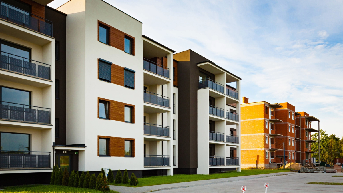 A modern multifamily housing complex with balconies and large windows, showing completed energy-efficient buildings next to new construction.