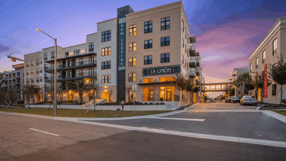 Exterior of La Unión Residences at Gasworx during sunset, with “Now Leasing” signage and connected buildings via skybridge.