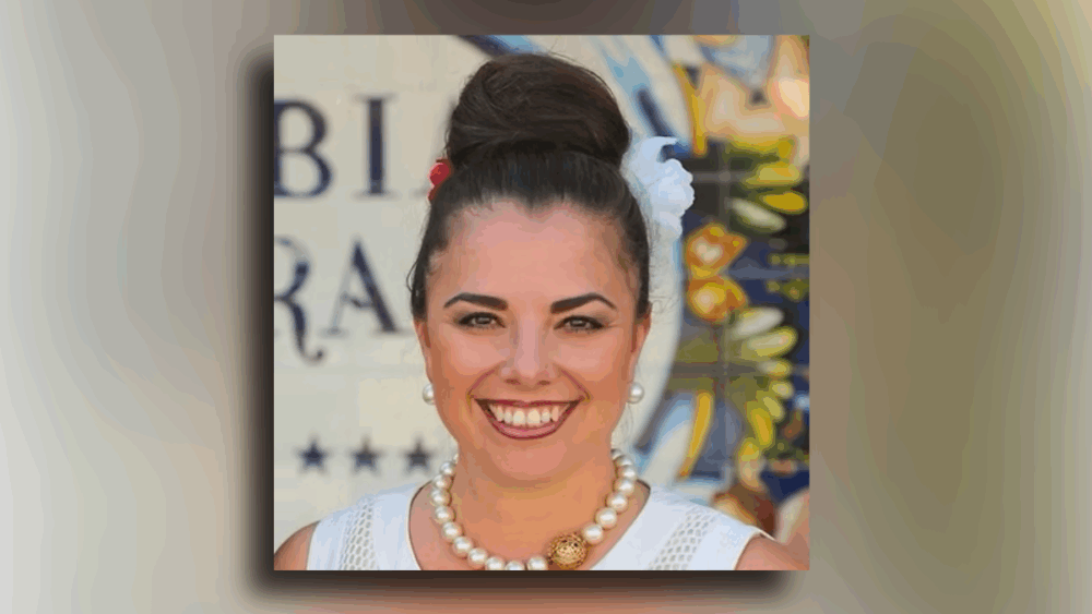 Andrea Gonzmart Williams, fifth-generation owner of Columbia Restaurant, smiling in a portrait with colorful Spanish tile in the background.