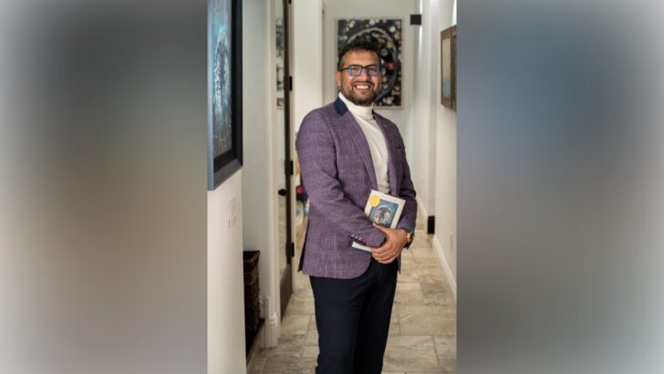 Dr. Ali standing in a hallway holding a book and smiling.