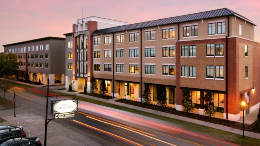 Exterior view of the Epicurean Hotel at sunset, showing the multi-story building with illuminated windows, brick and stucco design, street traffic light trails and a Bern’s Steak House valet parking sign in the foreground.