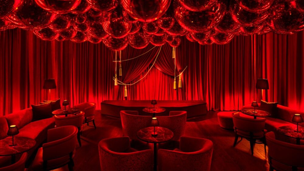Punch Room at The Tampa Edition featuring emerald velvet seating, warm lighting and lush tropical décor