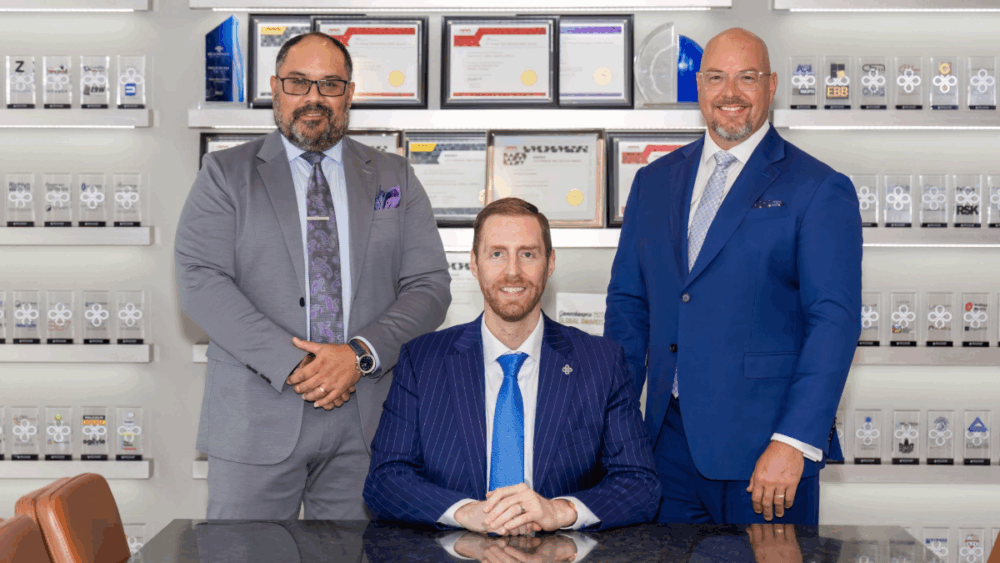 Three Benchmark International executives posing together in front of company awards display