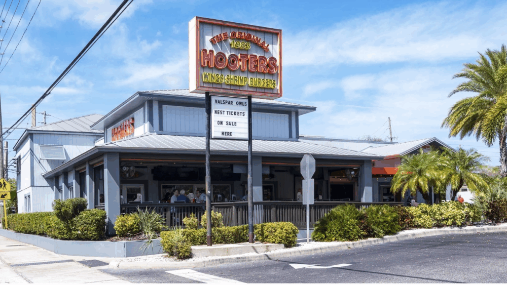 Exterior of the Original Hooters restaurant in Clearwater, Florida, featuring the 1983 sign above the entrance and palm trees surrounding the building.