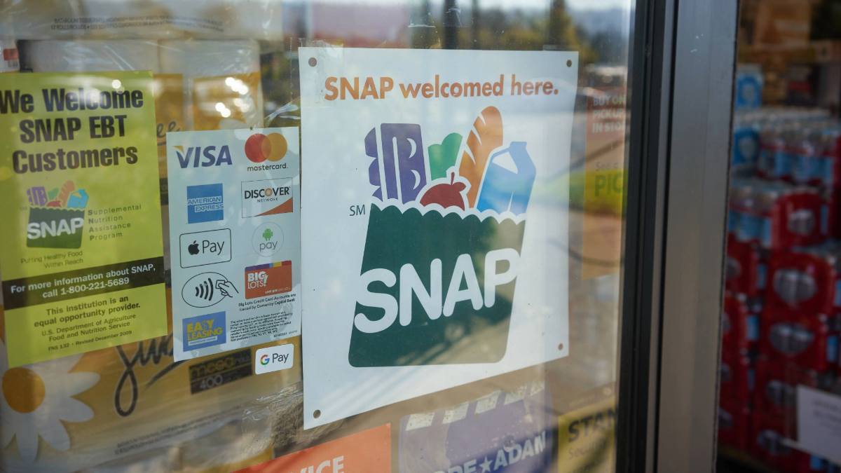Sign on a grocery store door reading “SNAP welcomed here,” showing that Supplemental Nutrition Assistance Program (SNAP) benefits are accepted for food purchases.