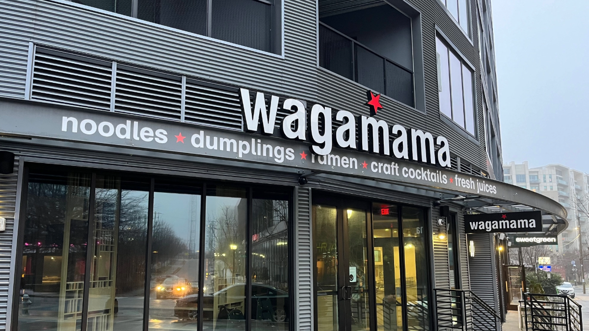 Exterior of a Wagamama restaurant with its name in bold lettering above the entrance, featuring signage for noodles, dumplings, ramen, craft cocktails and fresh juices.