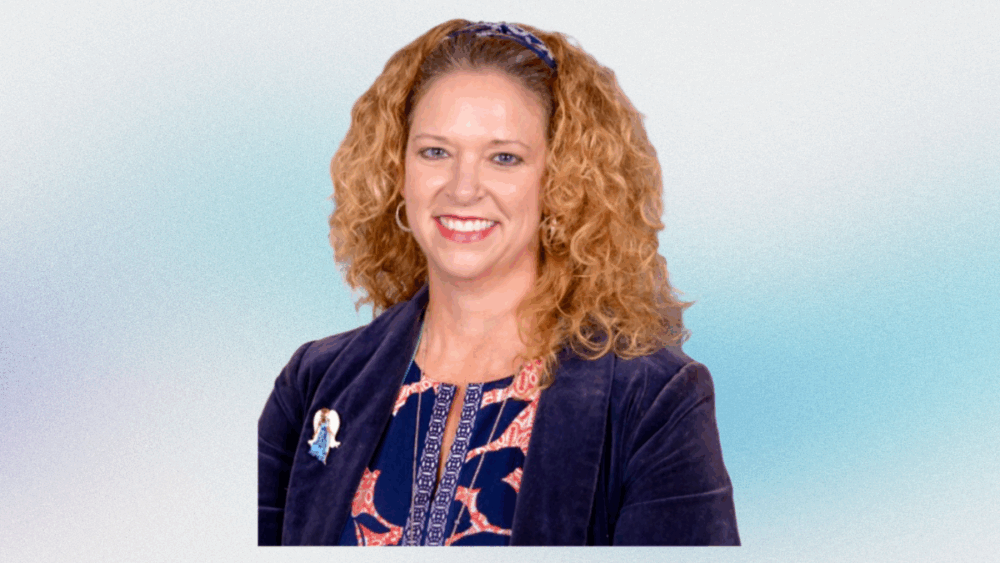 Portrait of Mandy Cloninger, the newly appointed CEO of Meals On Wheels of Tampa, smiling in a navy blazer and patterned blouse.