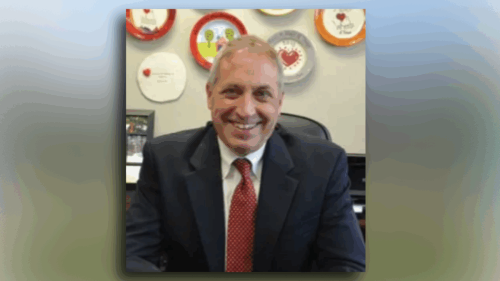 Steve King, outgoing CEO of Meals On Wheels of Tampa, smiling in his office with decorated plates featuring the organization’s heart logo behind him.