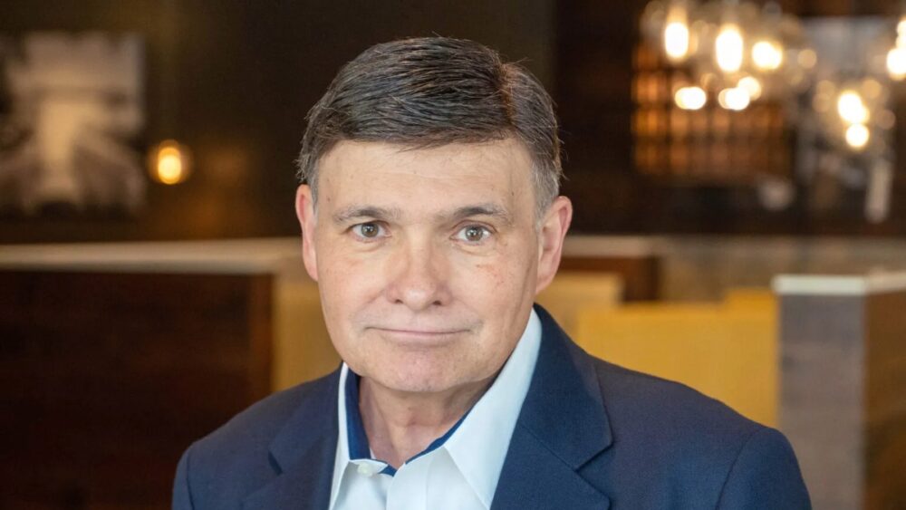 Headshot of Melting Pot CEO JC Crawford wearing a navy blazer and white shirt inside a warmly lit restaurant setting