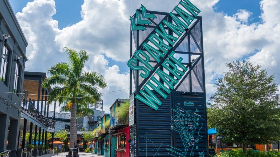 Sparkman Wharf in Tampa with its teal sign, palm trees and outdoor dining spaces on a bright sunny day.