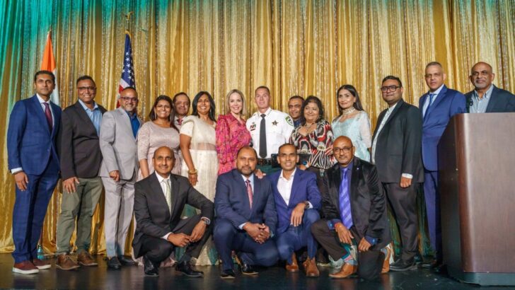 The full Sheriff’s Indian Advisory Council stands on stage with Sheriff Chad Chronister in front of gold drape backdrops.