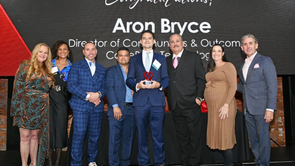 Group of eight people standing on stage at the Philanthropists of the Year Awards with honoree Aron Bryce holding his award.