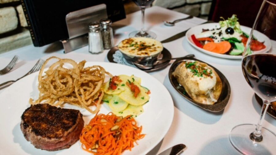 A plated steak dinner at Bern’s Steak House with French fried onions, vegetables, a baked potato and a glass of red wine.