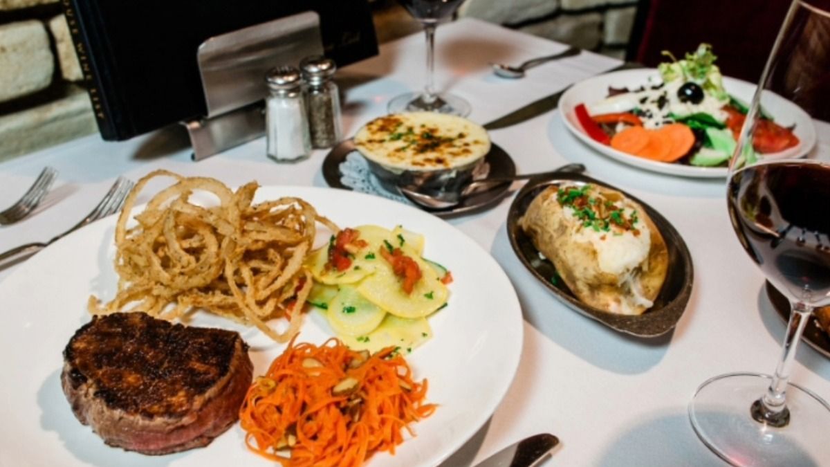 A plated steak dinner at Bern’s Steak House with French fried onions, vegetables, a baked potato and a glass of red wine.