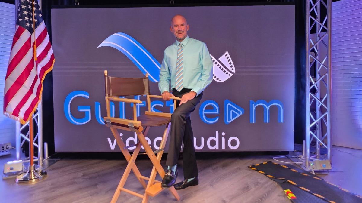 Chris Ingram sitting on a director chair in front of the Gulfstream Video Studio LED wall.