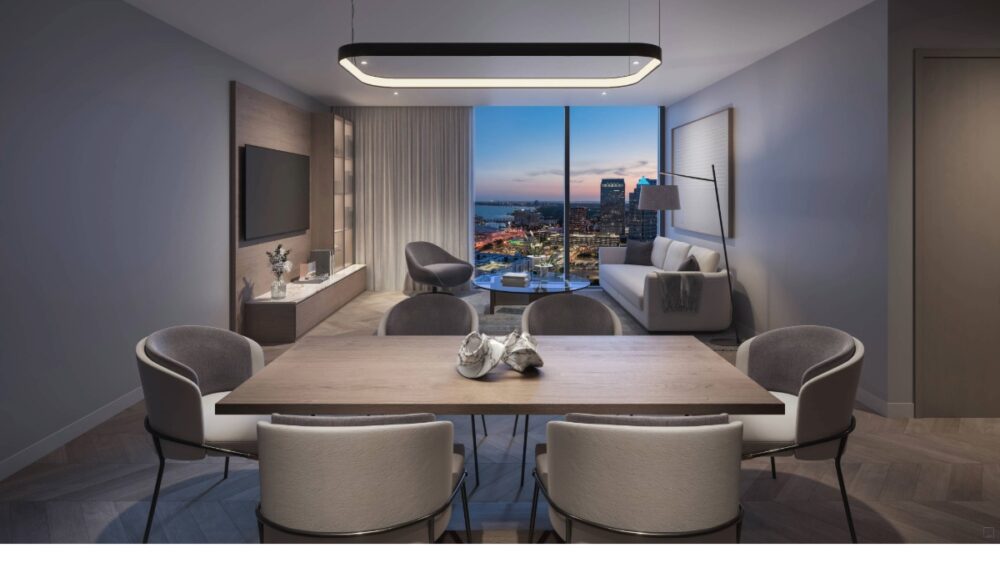Interior view of a Hotel ORA condo hotel unit with a dining table, living area and city skyline through floor to ceiling windows
