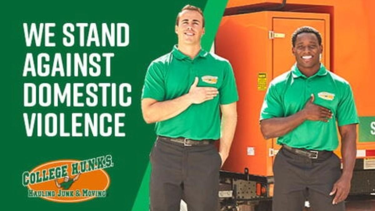 Two College HUNKS team members stand in front of a moving truck with their hands over their hearts beside text reading “We stand against domestic violence.”