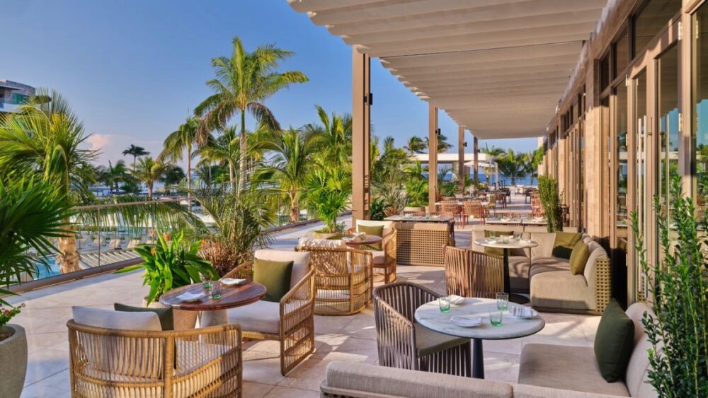 Outdoor dining terrace at the St. Regis Longboat Key surrounded by palm trees with views of the pools and Gulf.