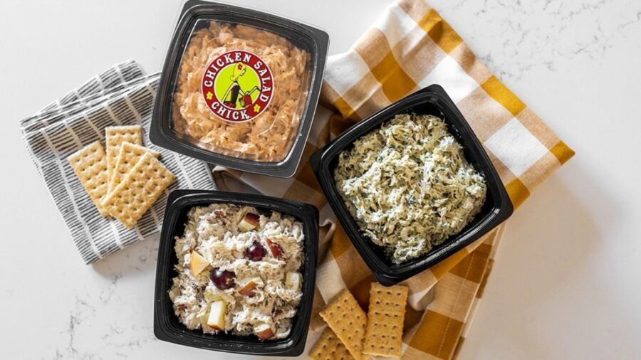 Three containers of Chicken Salad Chick’s signature chicken salad flavors arranged on a kitchen counter with crackers.