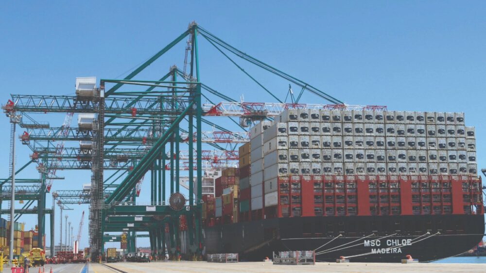 A large Maersk container ship docked at a port with multiple Liebherr ship-to-shore cranes loading and unloading cargo under a clear blue sky.